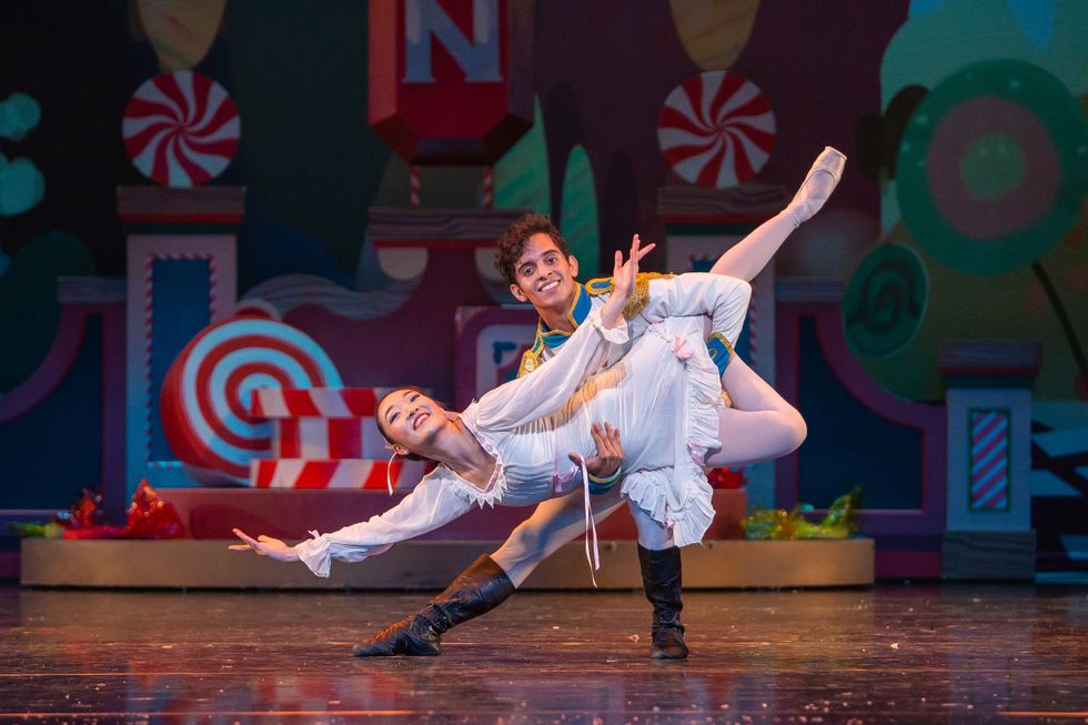 In front of a backdrop of life-sized candy, Alejandro Gonzalez, who wears a prince costume, holds Mayu Odaka, who wears a white nightgown, in a fish lift.