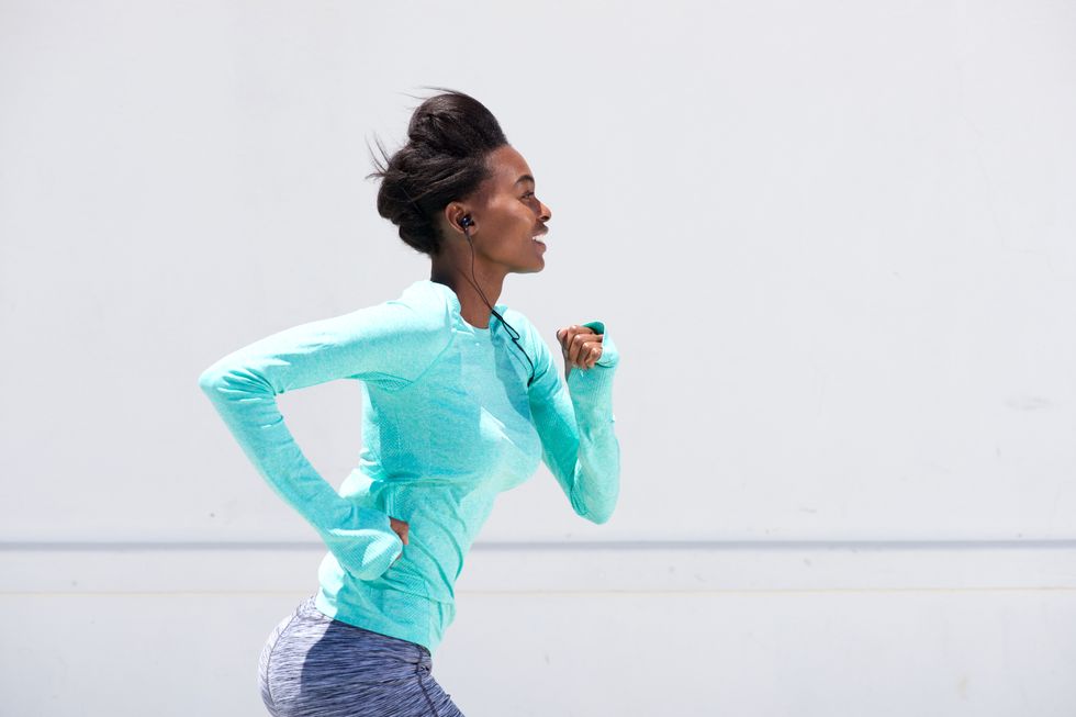 Young woman in green and blue running outside with headphones