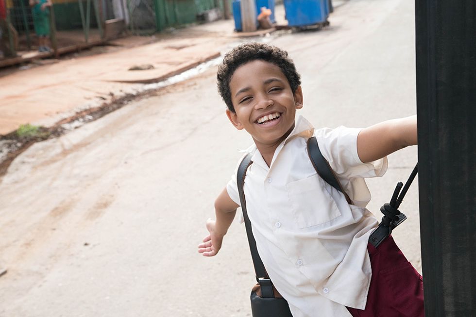 Edlison Manuel Olbera Nu00fau00f1ez, playing a young Carlos Acosta in Yuli, grins as he hitches a ride on the side of a moving bus.