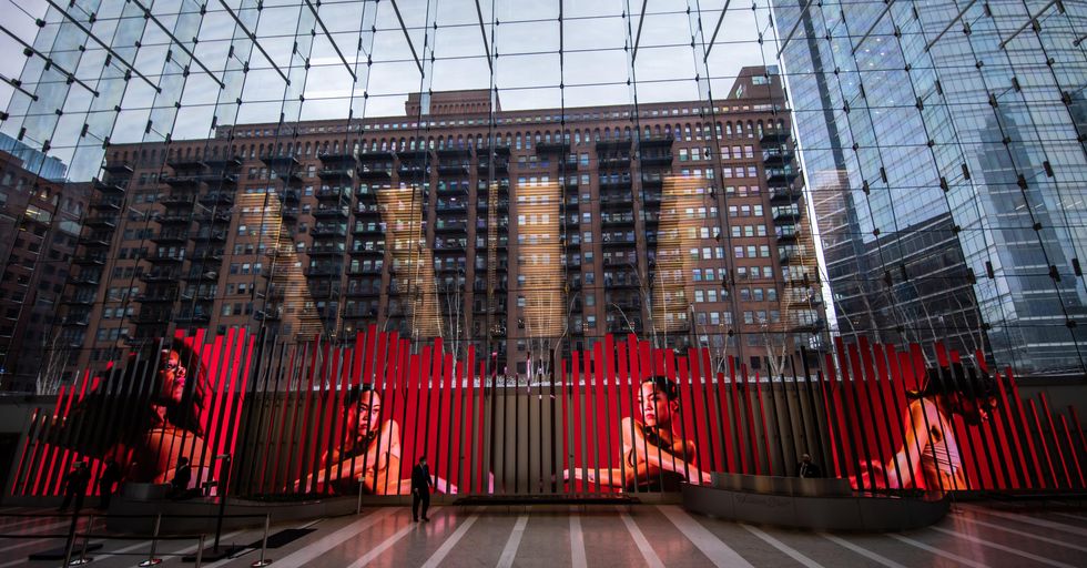 In the glass lobby of a building, a panel of LED blades stretches along the wall and features a film showing the images of four female dancers from the waist up.