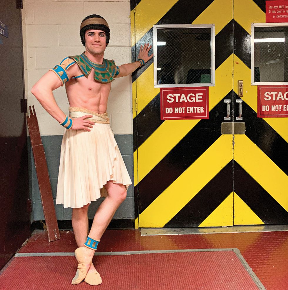 Campbell in a gladiator costume and skirt leaning in front of a backstage door.