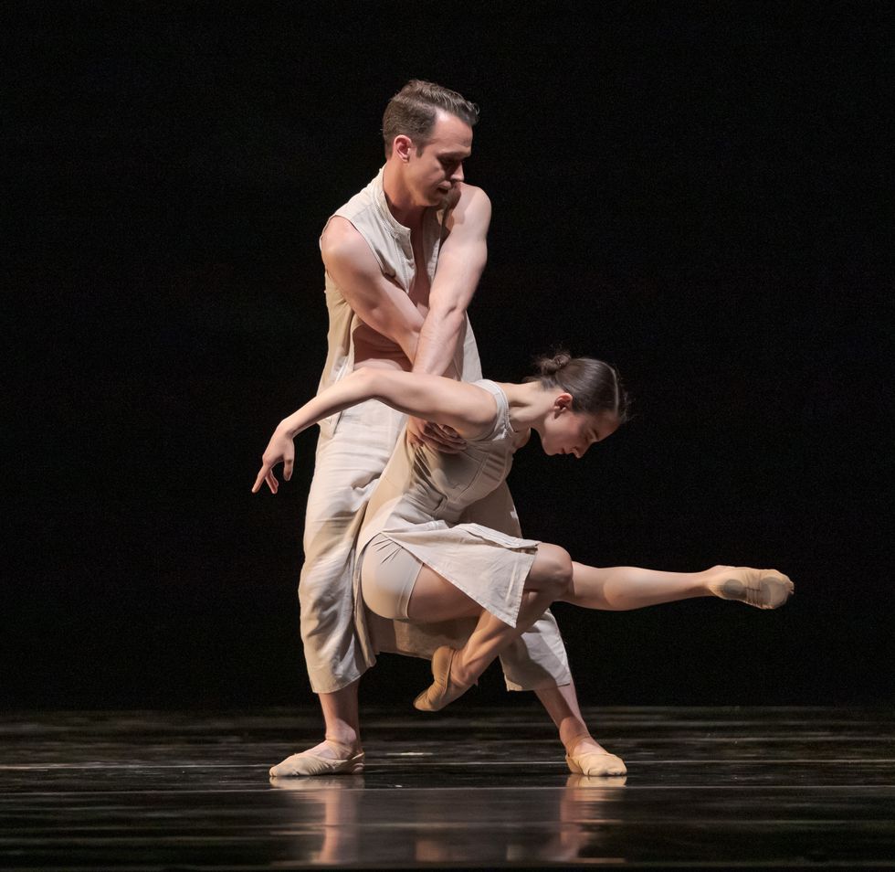 Wearing white skirted costumes, Ben Needham-Wood crosses his arms and lifts Terez Dean by the shoulders as she extends her left leg straight in front of her and tucks her right leg underneath her.