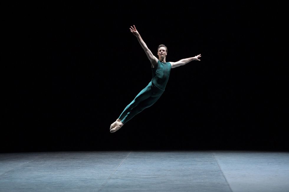 Wearing green tights and tight green T-shirt, James Streeter jumps up in fifth position with his arms up in a V-shape.
