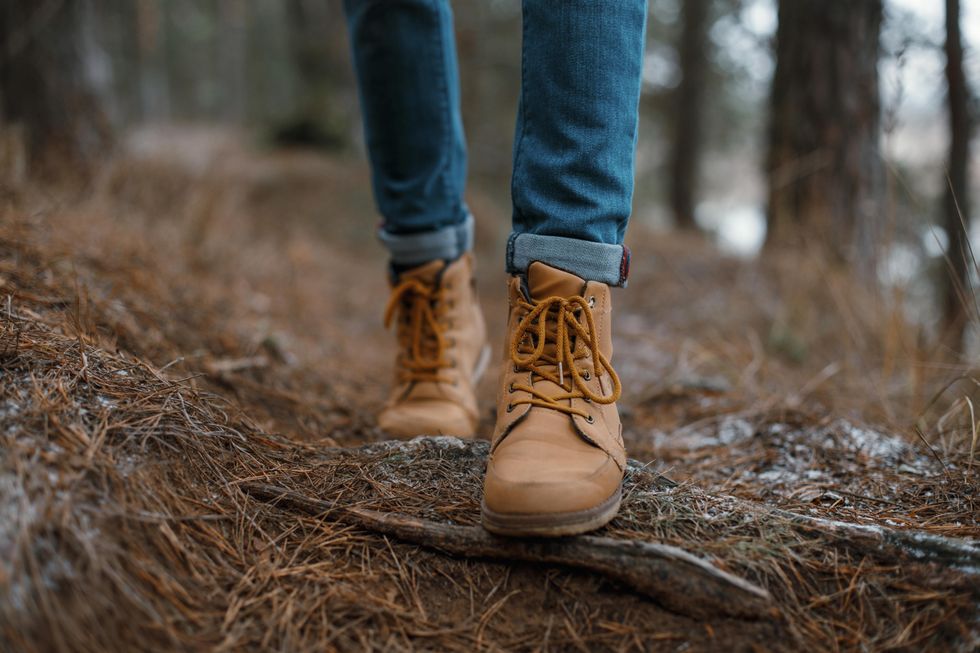 An image from the ankles down of someone in jeans and tan boots walking on a bed of pine needles.
