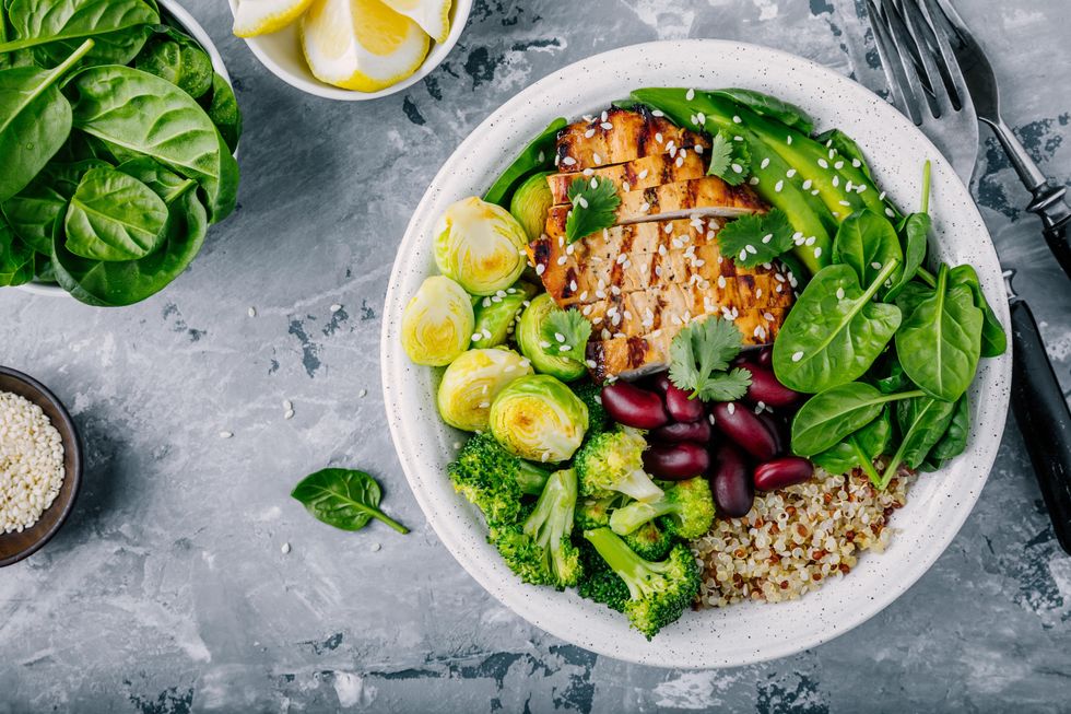 A grain bowl with quinoa, grill chicken strips, broccoli, Brussels sprouts, kidney beans and spinach.