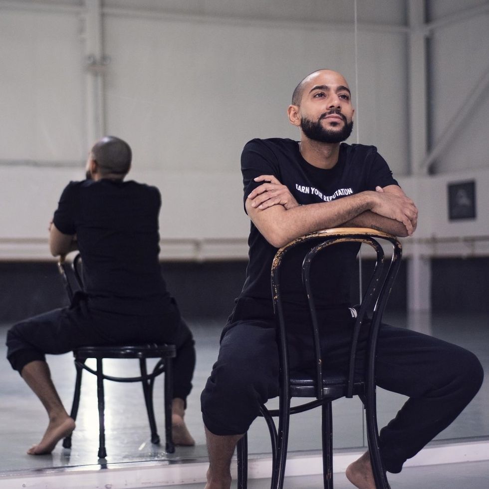 Miller sits backwards on a chair, his arms folded, in a dance studio