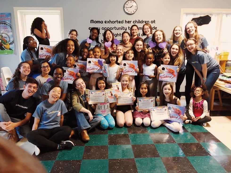 A classroom full of school children and young adult volunteers pose and smile for the camera. Some holding the book Firebird while others hold cut-out paper hearts or certificates.