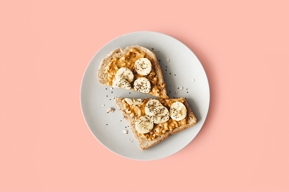 Bananas and peanut butter and chia seeds on toast on a white plate against a pink background.