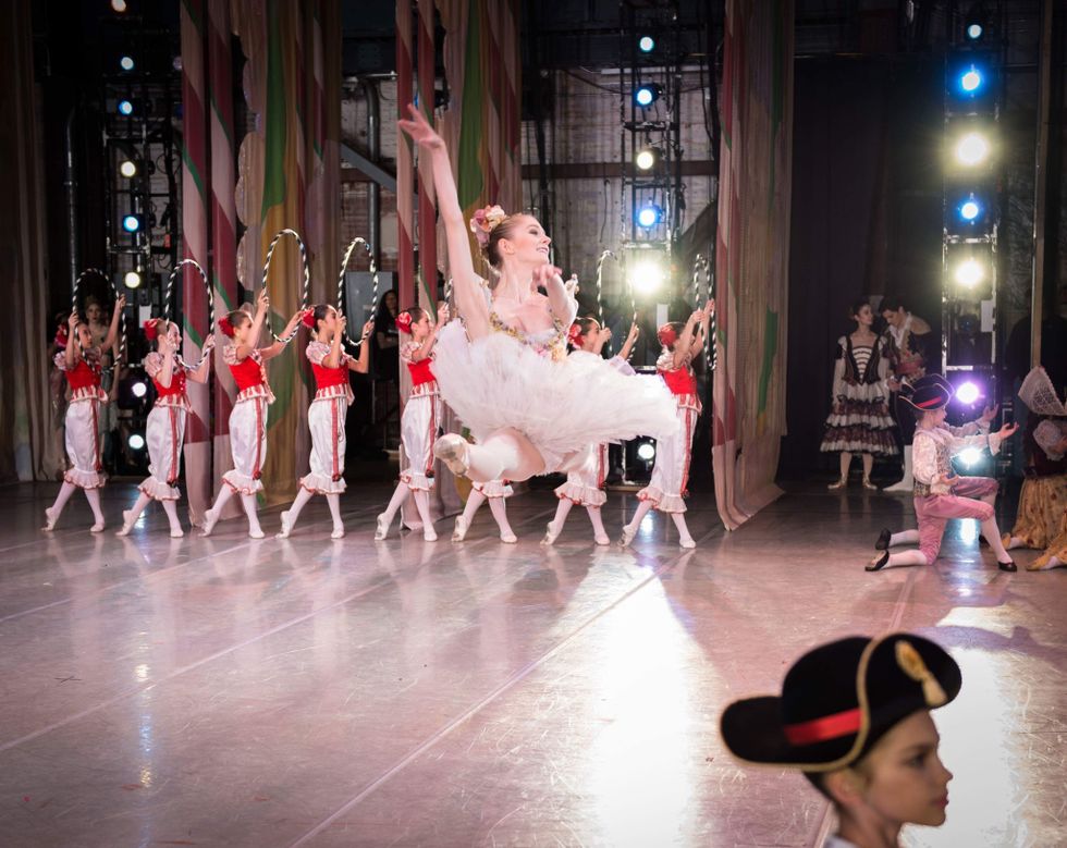 Dressed in a pink tutu, Jacqueline Callahan leaps across a brightly lit stage, surrounded by children costumed as Nutcracker characters.