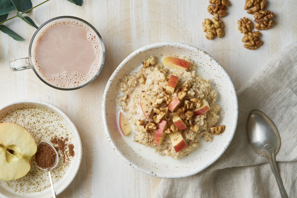 Bowl of oatmeal with apples on a linen placemat. Next to it is a cup of tea and another bowl with chia pudding and an apple.