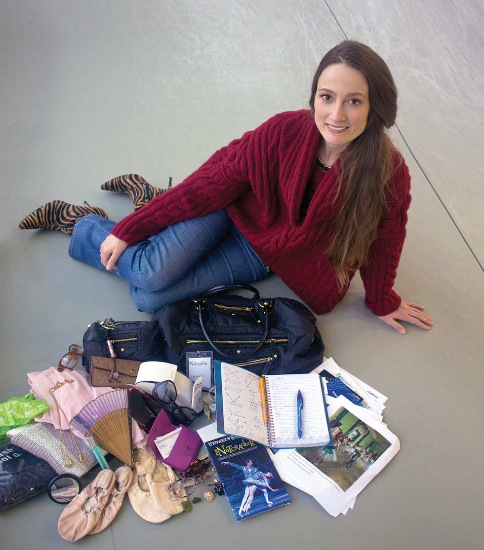 Julia Kent in a red sweater, jeans and tiger print boots poses in a dance studio behind the contents of her bag. Photo is taken from above.