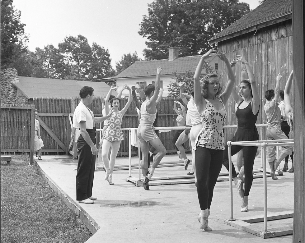 Black and a white photograph of dancers at the barre, outside, in floral practice clothes.