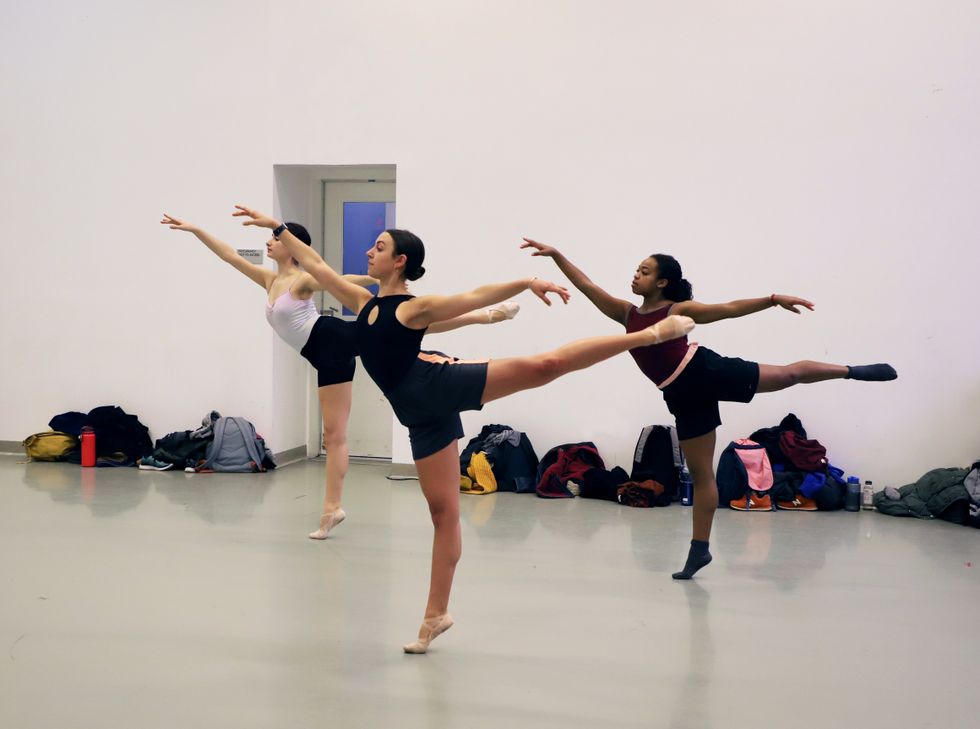 Three female ballet dancers perform arabesque in ballet class