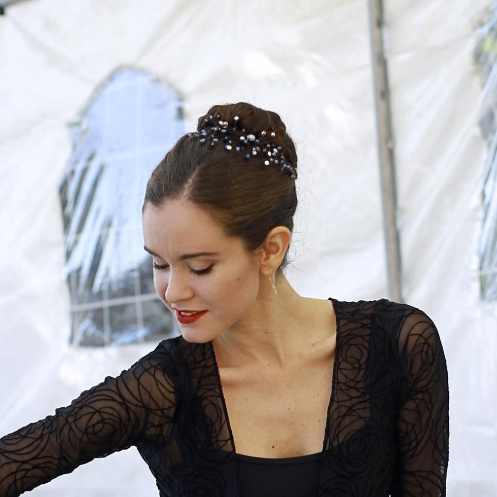 A ballerina in a black leotard with her dark hair upswept in a high French twist looks down and smiles, showing off a sparkly blue and silver hair comb on the left side of her twist.