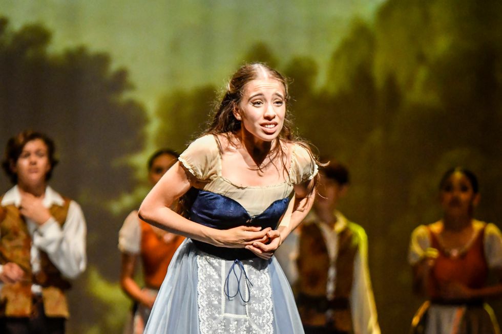 Wearing a blue peasant dress, Margarita clutches her heart and makes a pained face onstage.