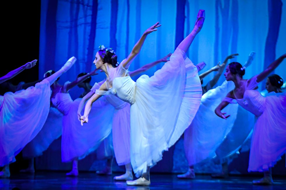 Margarida Gonçalves, dressed in a romantic white tutu, does a penché arabesque her right leg. A corps of girls in similar costumes do the same behind her.