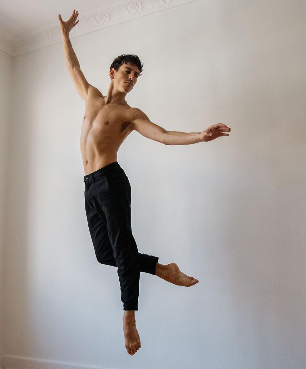 Vincenzo Di Primo, a tanned male dancer wearing black trousers, seems to float against a white background, head inclined toward his left leg as it bends in a slight attitude.