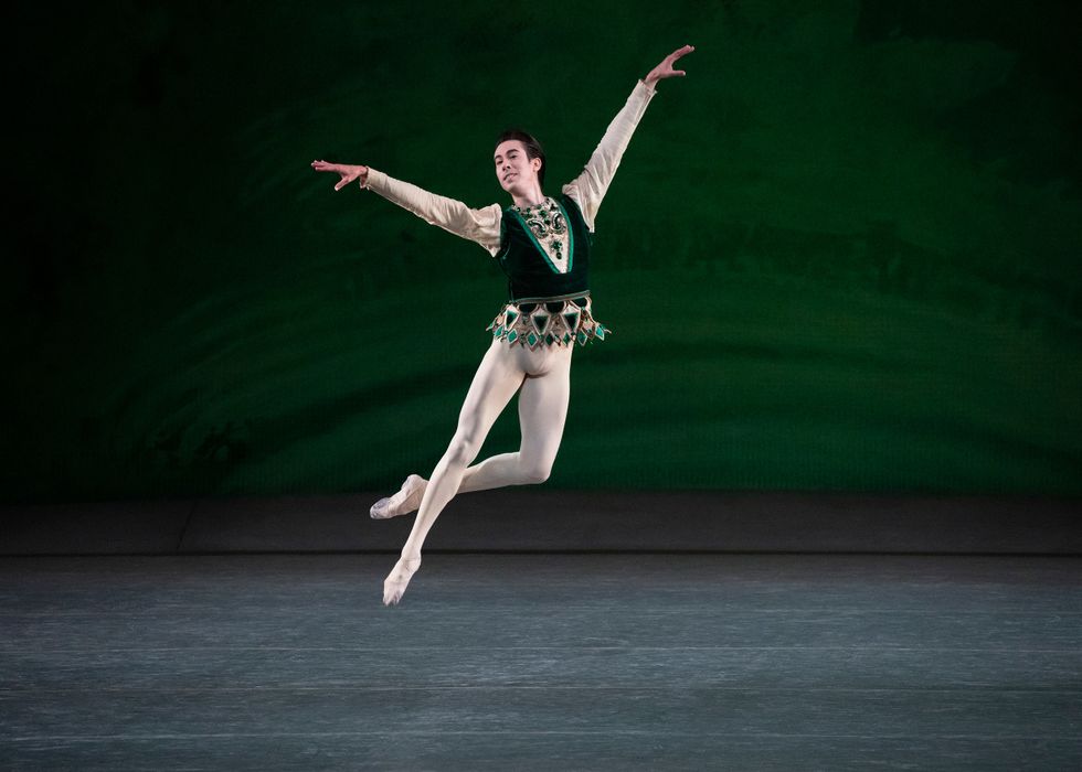Applebaum jumps in the air in a green velvet vest against a green painted backdrop