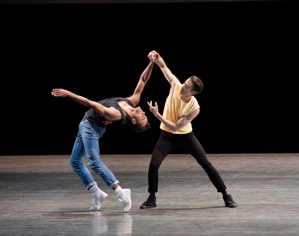 Applebaum, in black pants, sneakers and a yellow t shirt, guides Stanley with his arm, as Stanley leans into a backbend in jeans and white sneakers.