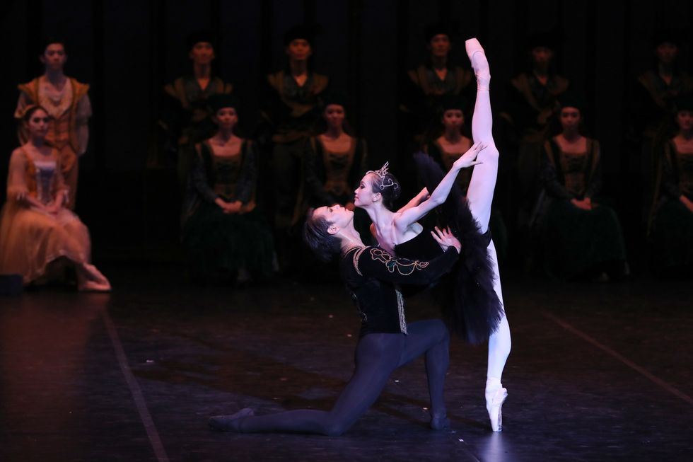 Husheng, dressed in a princely velvet jackets and black tights, supports Bingxue in an over extended penchu00e9. She's wearing a black Odile tutu and crown.