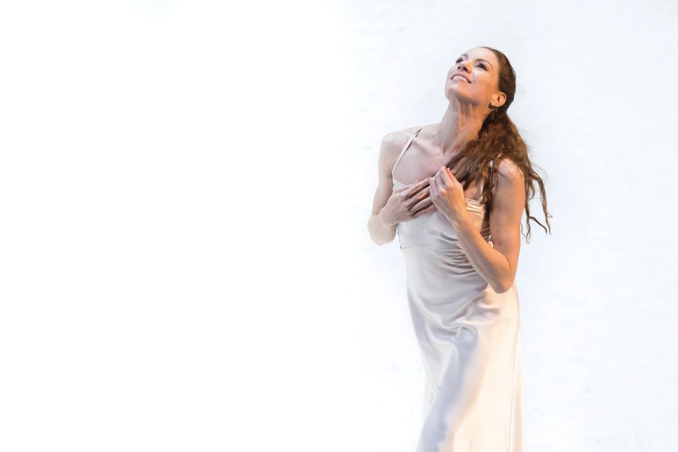 April Ball in a white dress against a white background, with her hands on her chest.