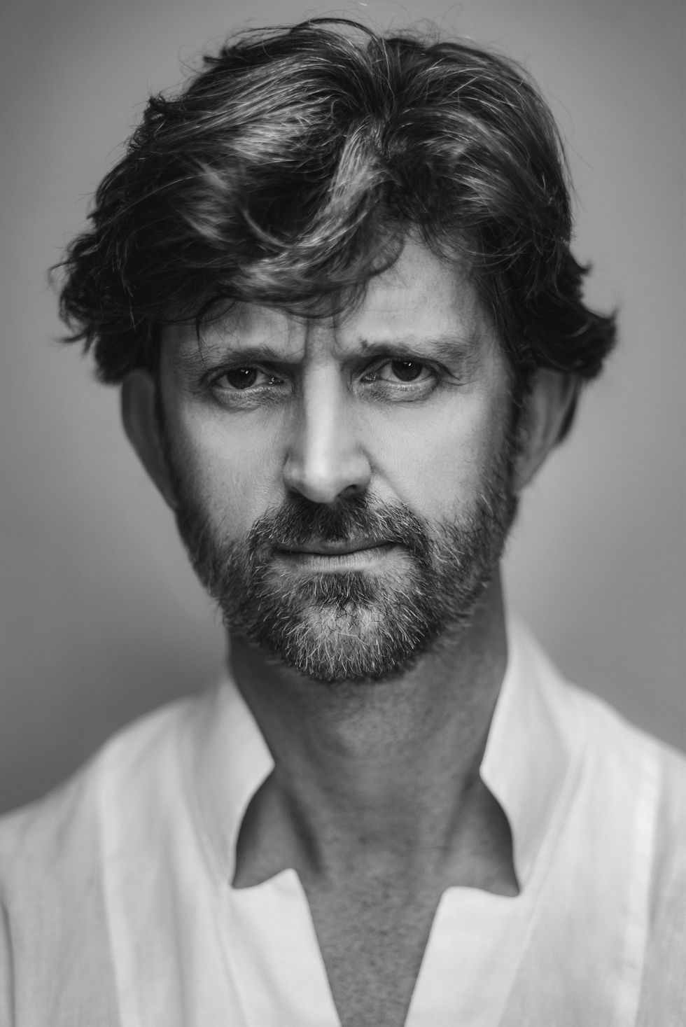 Paul Lightfoot wears a white button-down shirt and smiles directly towards the camera in a black and white portrait shot.