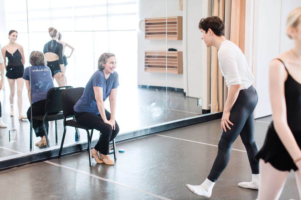 Ringer sits on a chair at the front of a studio while dancers come up to her.