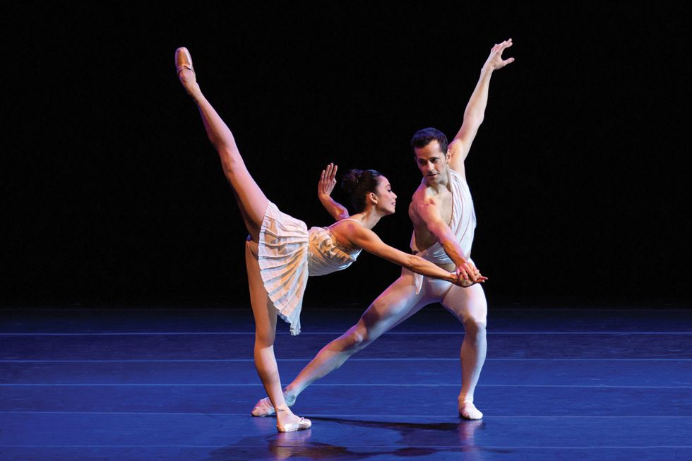 Fairchild onstage in white tights leans to the left while holding the hand of Abrera, in a penchu00e9 in a white pleated dress.