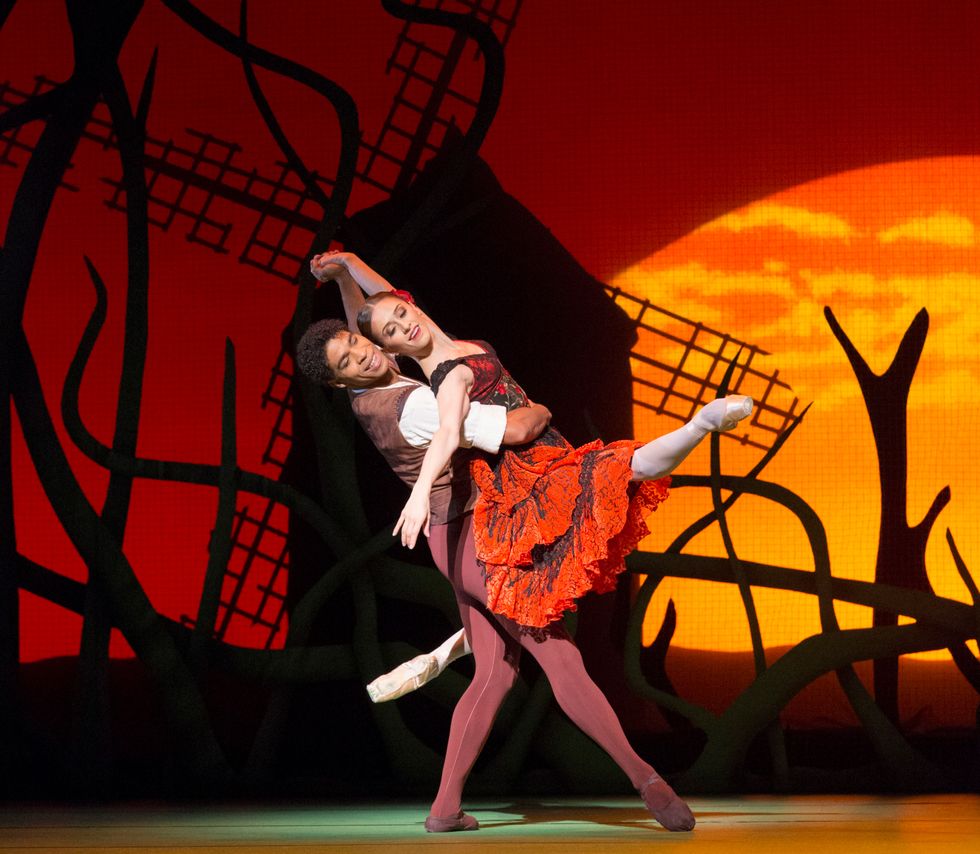 Nuu00f1ez dressed in red as Kitri, held by Carlos Acosta against a windmill background onstage