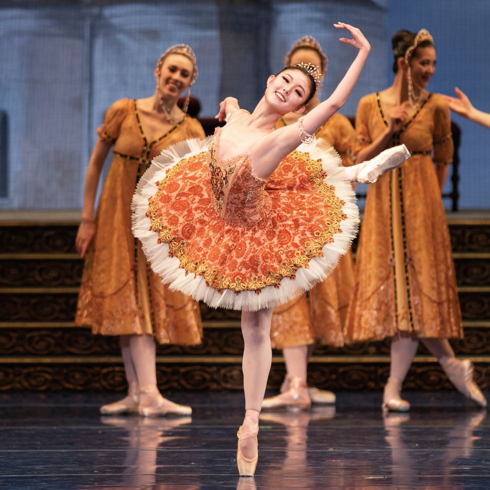 Wona Park, smiling in a ranversu00e9 onstage, wearing an orange tutu and gold crown.