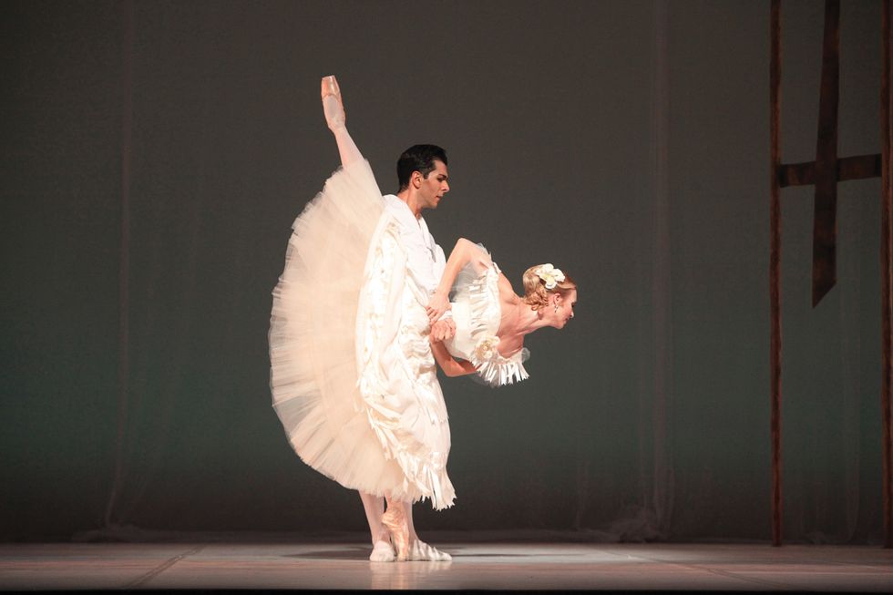 Hulland is onstage in an arabesque penchu00e9 with Graziano's arms around her waist. They both wear all white costumes.