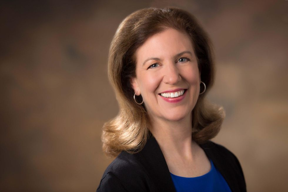 Darleen Callaghan, shown from the chest up and wearing her brown shoulder-length hair long, smiles happily toward the camera in front of a brown backdrop.