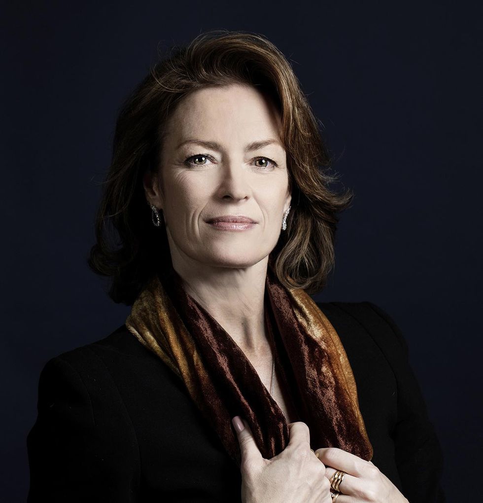Kathryn Bradney, a middle-aged white woman with brown, bobbed hair and wearing a black velvet top, offers a small smile to the camera while touching the brown velvet scarf draped around her shoulders.