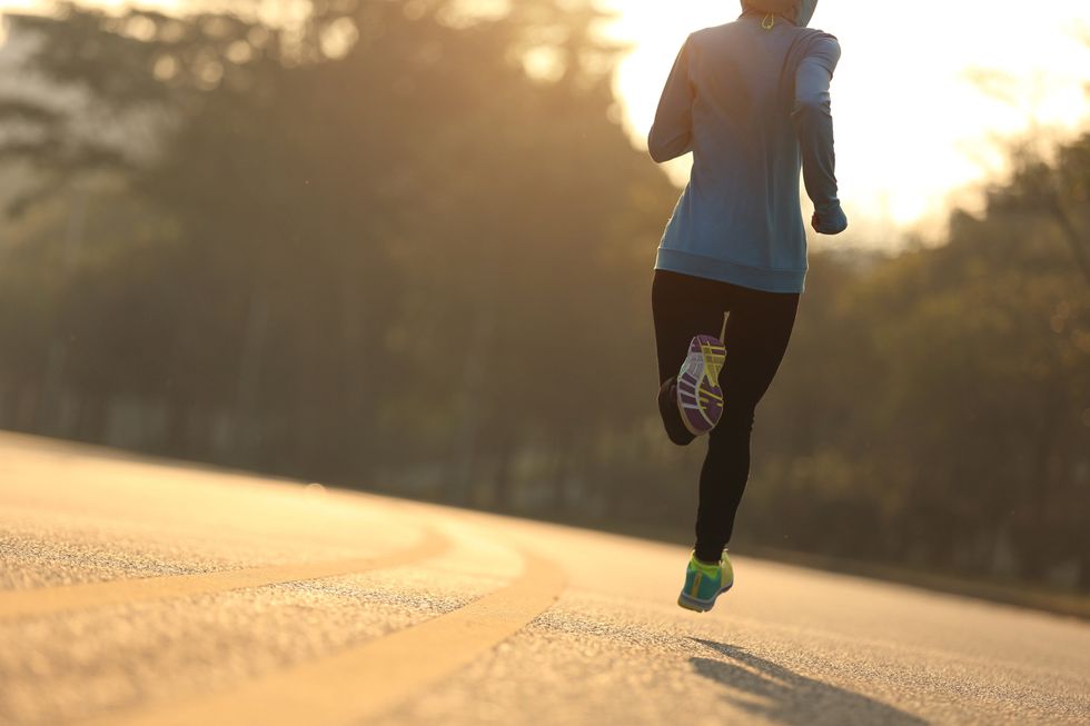 A woman runs on a deserted street, with trees on either side.
