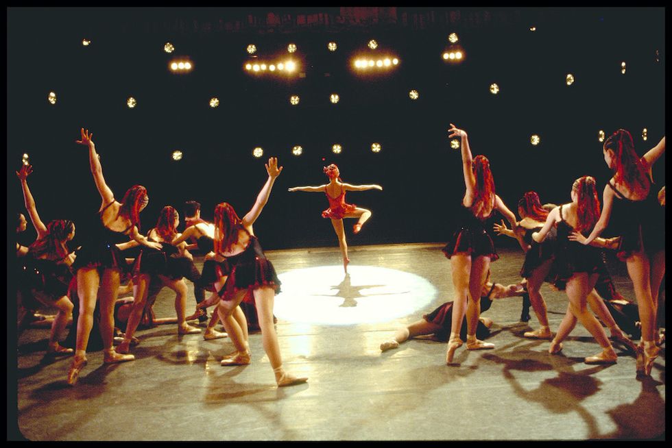 A still from "Center Stage." Schull is in the center of the stage, in a spotlight, mid-fouettu00e9. We see her, and the other dancers in the scene, from behind.