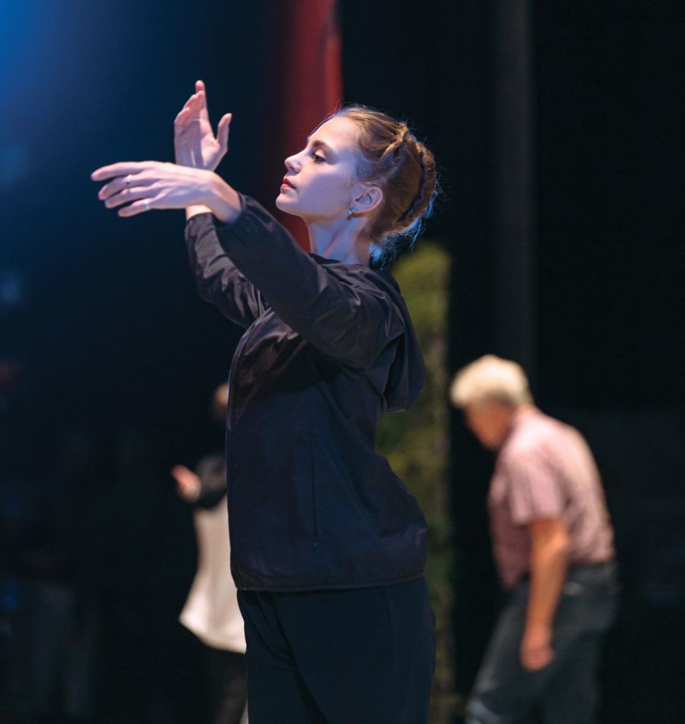 Ionova in dark pants and a warm-up jacket, gestures onstage in rehearsal.