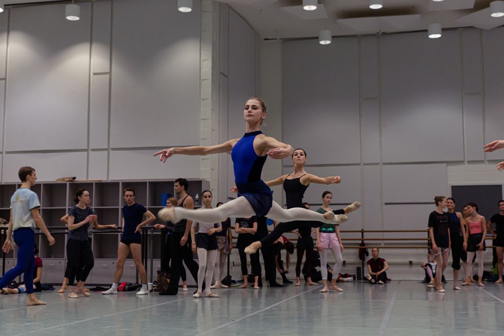 Daria Ionova, in a blue leotard and pink tights, leaps across the studio in class.
