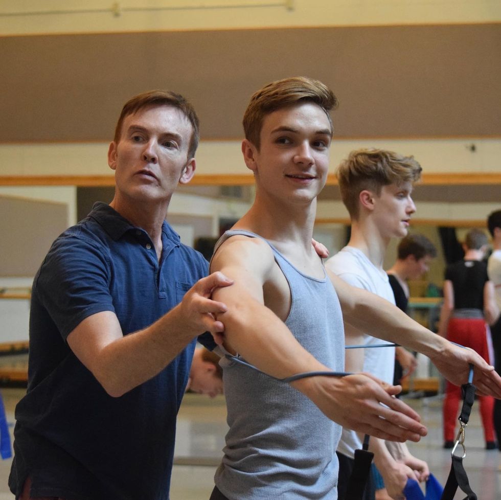 Christopher Alloways-Ramsey adjusts the arm of a young male dancer during a ballet class.