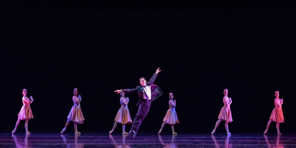 Antonio u200bMorillo, in a tuxedo, does an assemblu00e9, while six women in pastel dresses and pointe shoes stand behind him in tendu derriu00e8re.