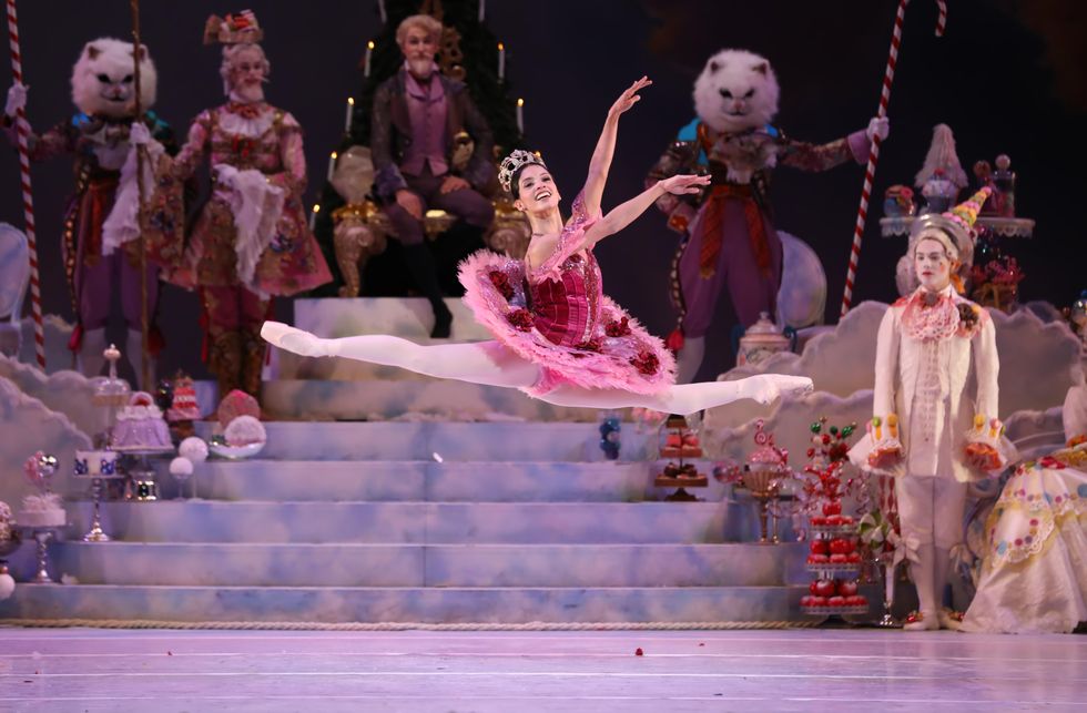 Karina Gonzu00e1lez jumps across a stage, wearing a pink tutu and a crown