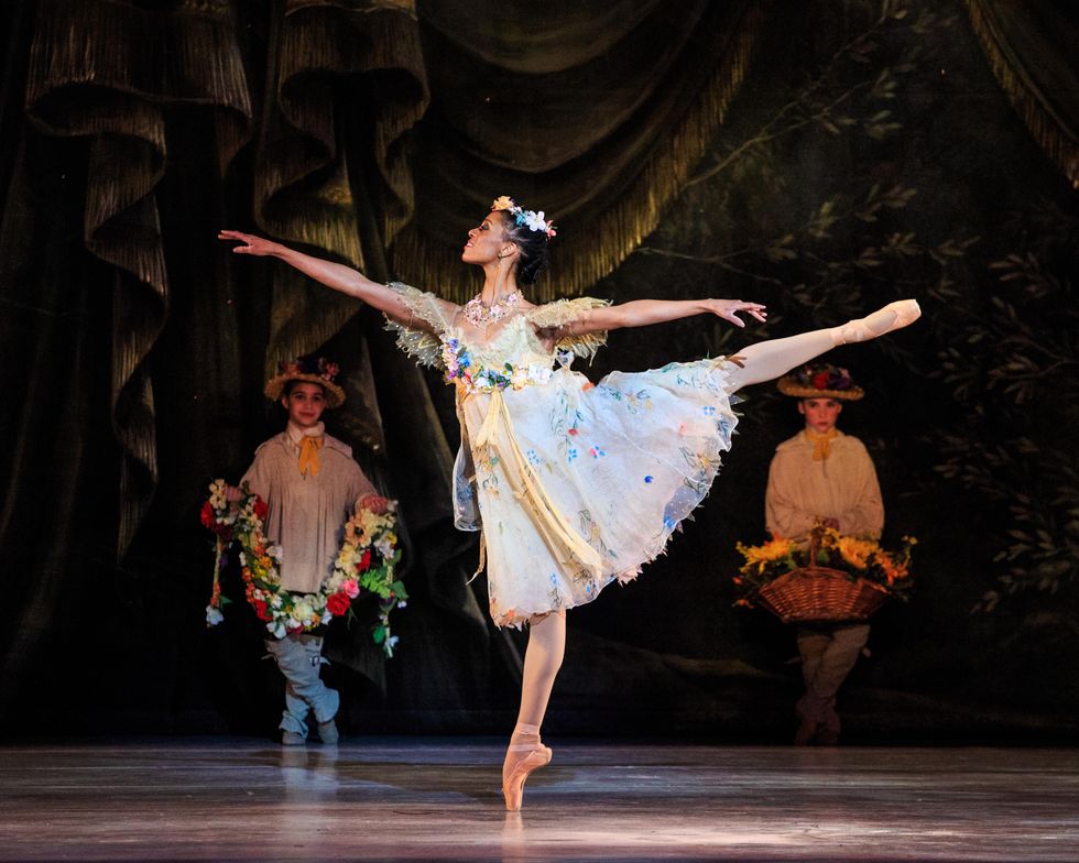 Katlyn Addison poses onstage in arabesque en pointe, with two children holding flowers