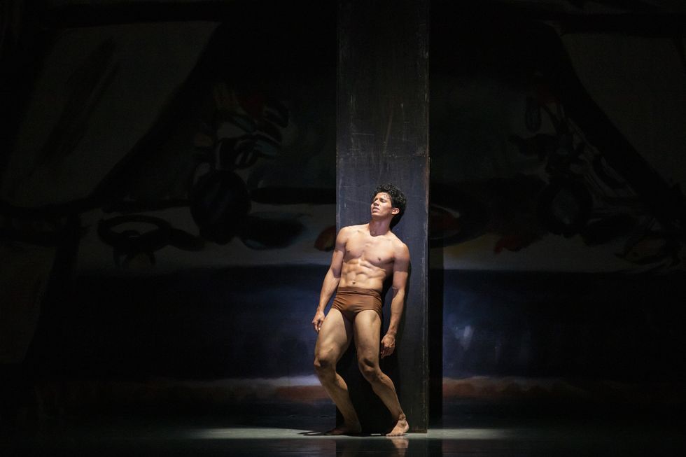 Wearing only brown trunks, Hadriel Diniz slumps against a pillar in agony, bathed in a bright spotlight.