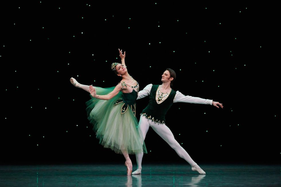 Wearing a long, green Romantic tutu, Sasha Mukamedov does a high croisu00e9 arabesque with her arms moving out towards her sides. Aaron Robison, wearing a dark green velvet tunic and white tights, lunges right and holds onto her waist with his right hand, with his left arm out to the side.