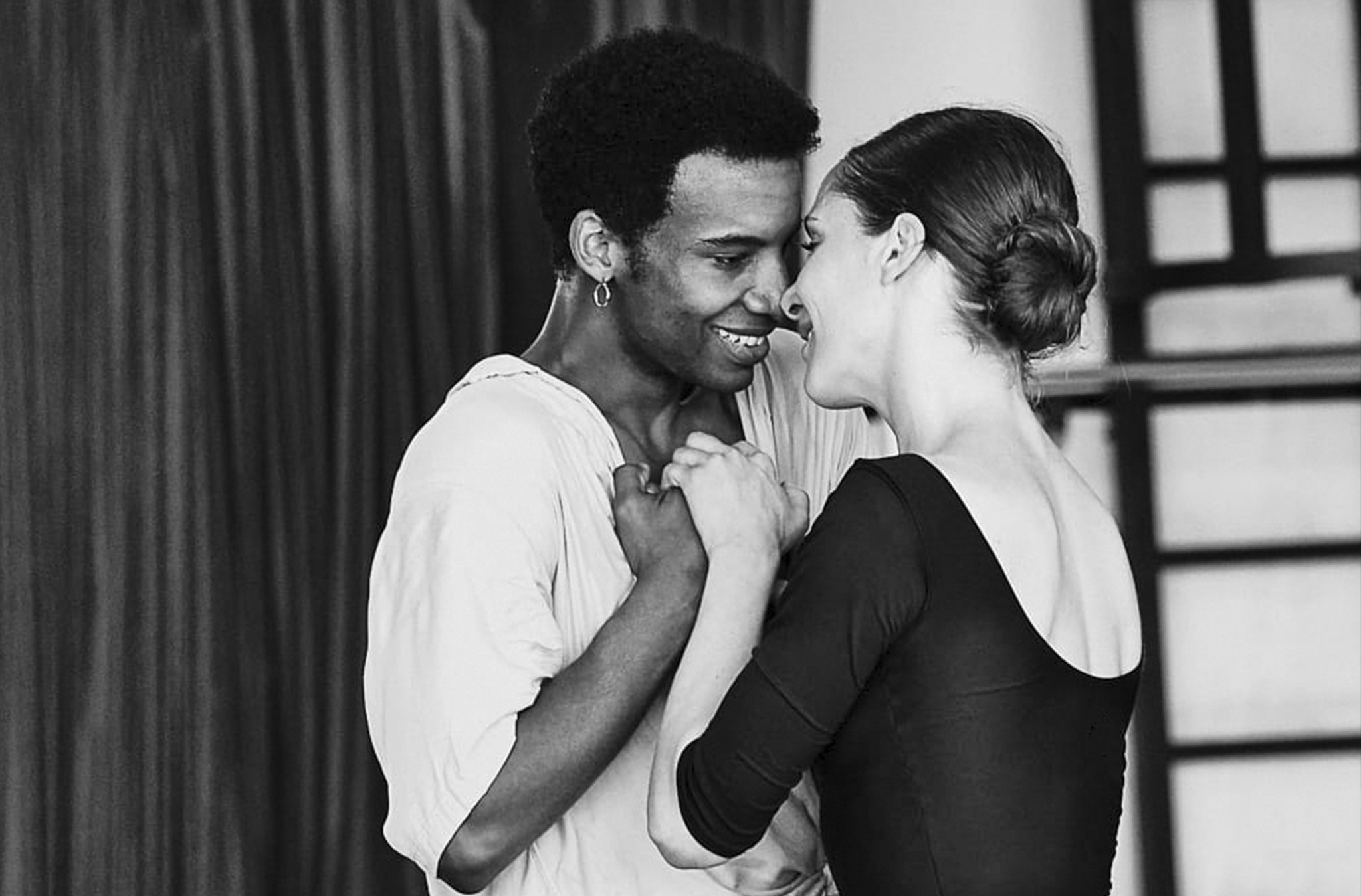 A black and white photo of Osiel Gouneo and Valentine Colasante embracing, in character, in rehearsal.