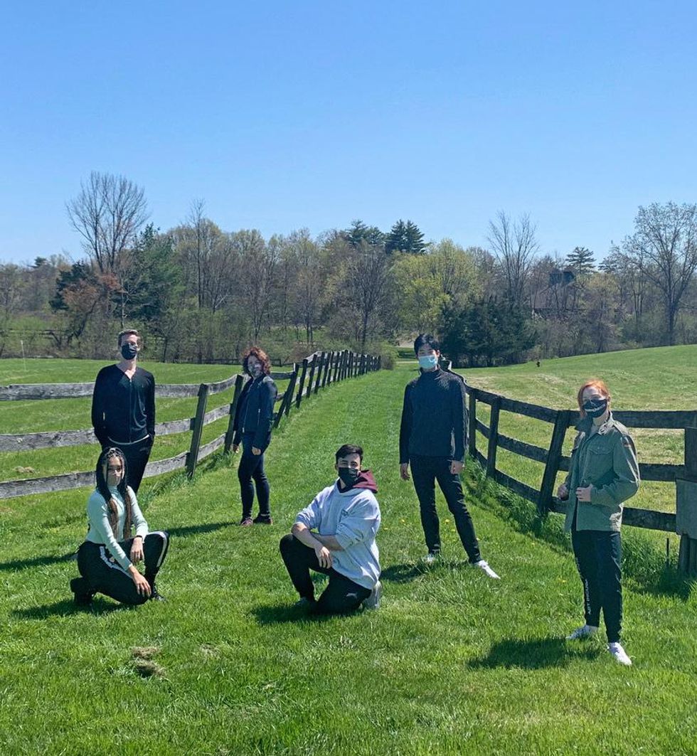 A group of six peopleu2014three men and three womenu2014pose on a grassy field between two wooden fences, posing in jackets and assorted athleisure.