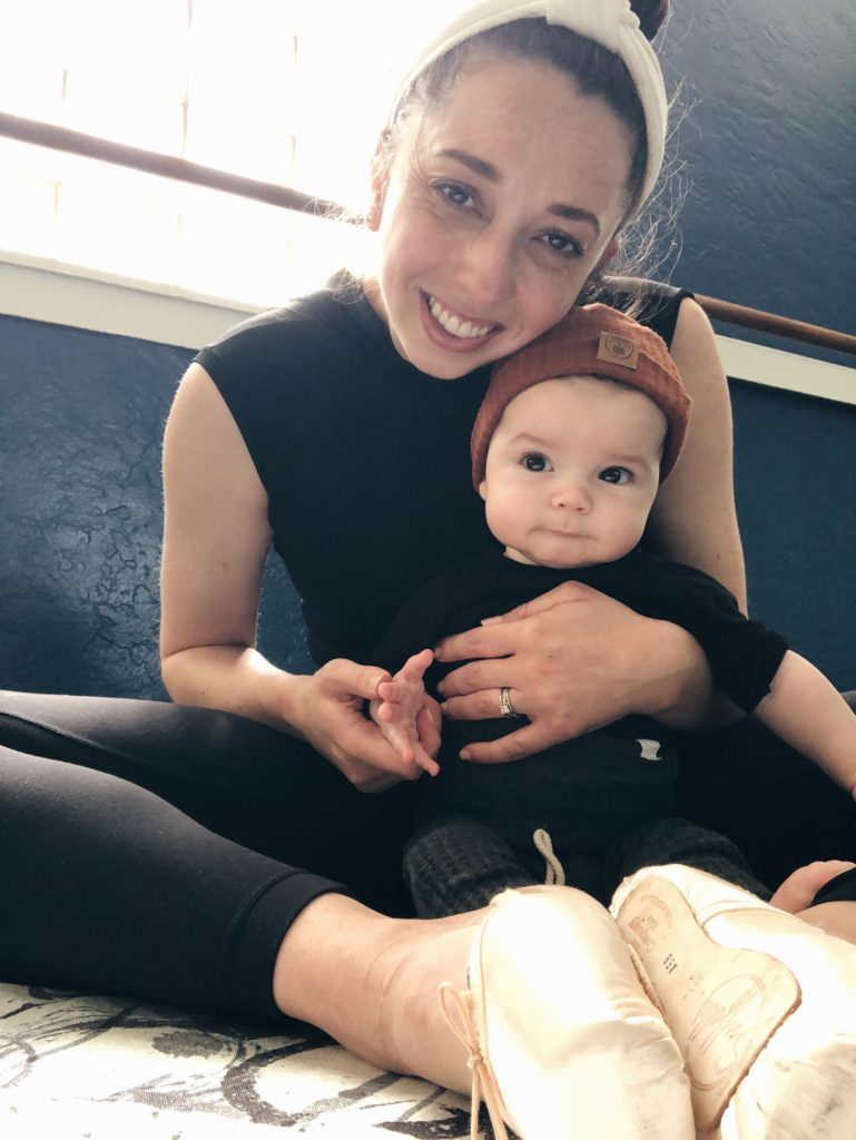Jordan Nicole Tilton sits in black leggings with a high-necked, black leotard and satin pointe shoes. She holds her son, Rocco in her lap.