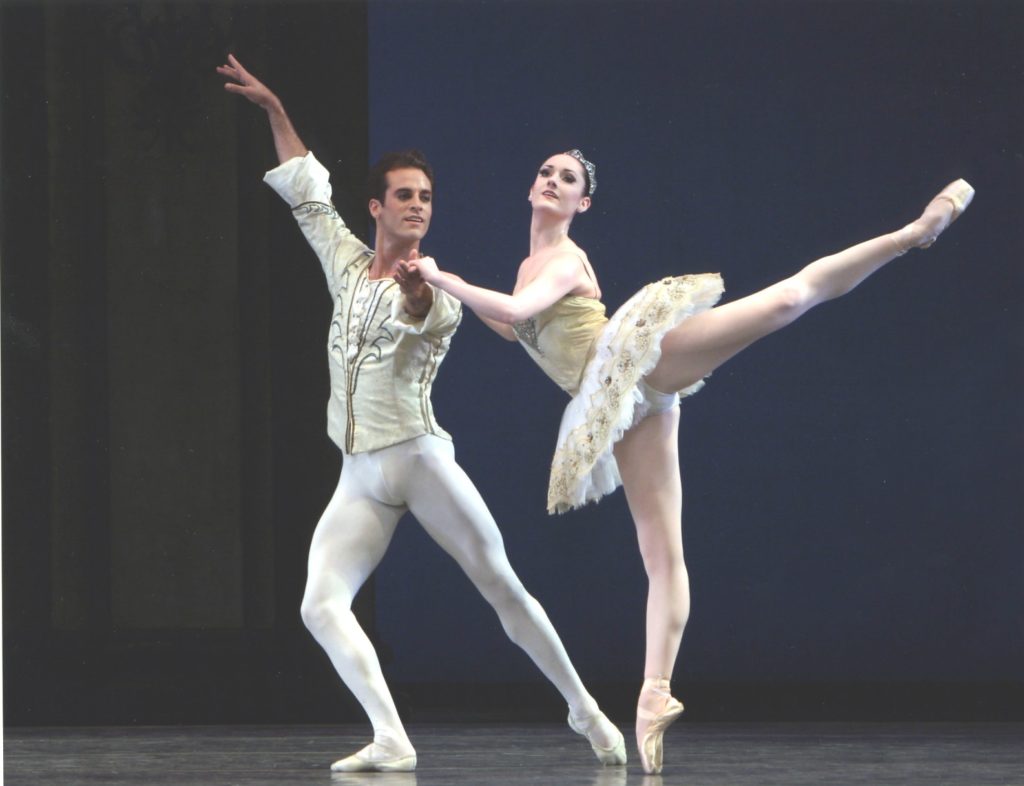 Benjamin Millepied lunges to his right and holds his left arm out while Miranda Weese holds his left hand and shoulder to balance in arabesque. He wears white tights and slippers and a white tunic and she wears a white tutu, tiara, pink tights and pointe shoes.