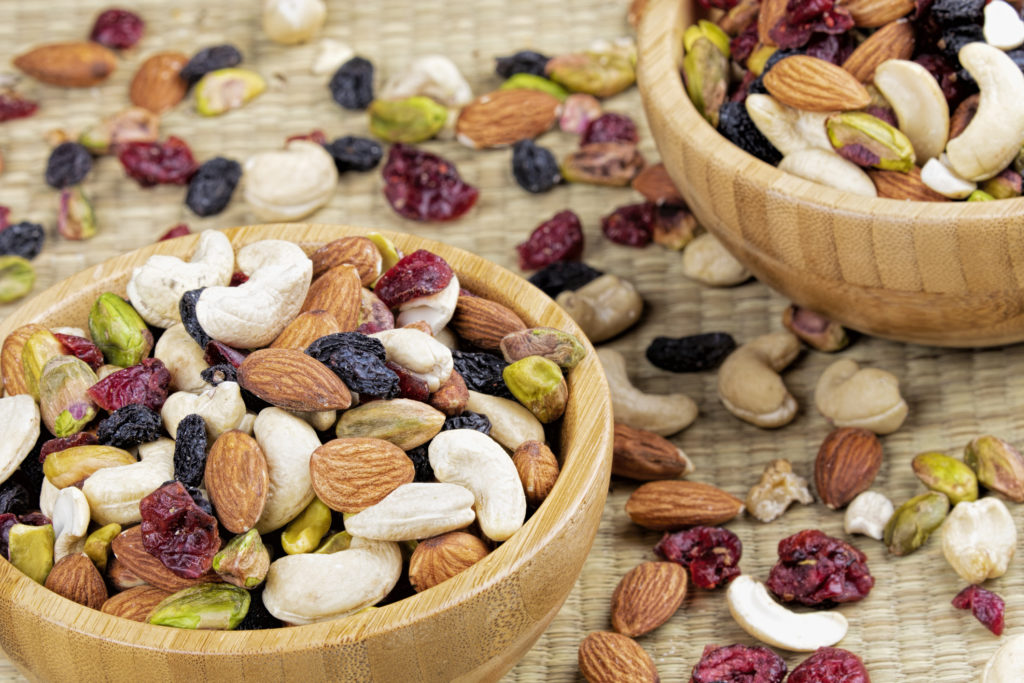 Trail mix in two small wooden bowls and scattered around the bowls. A mixture of nuts and dried fruit.