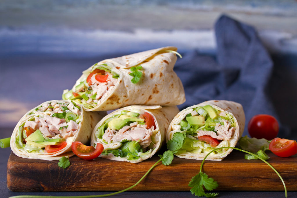 Turkey wraps with avocado, tomatoes and iceberg lettuce on chopping board