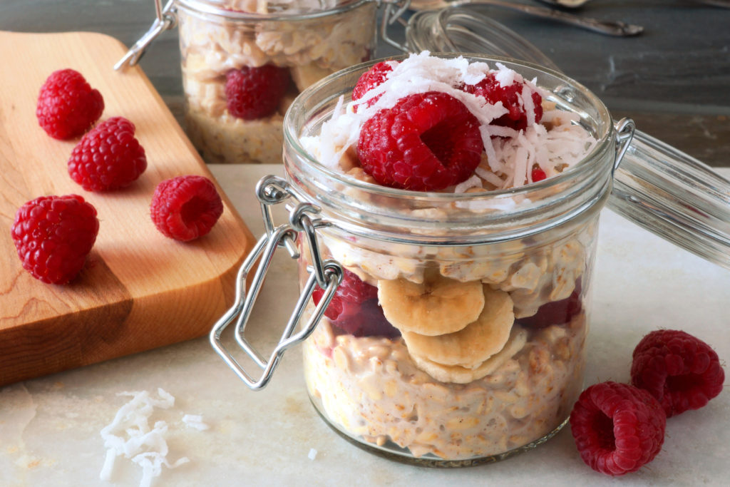 A glass jar of overnight oats topped with raspberries and shredded coconut